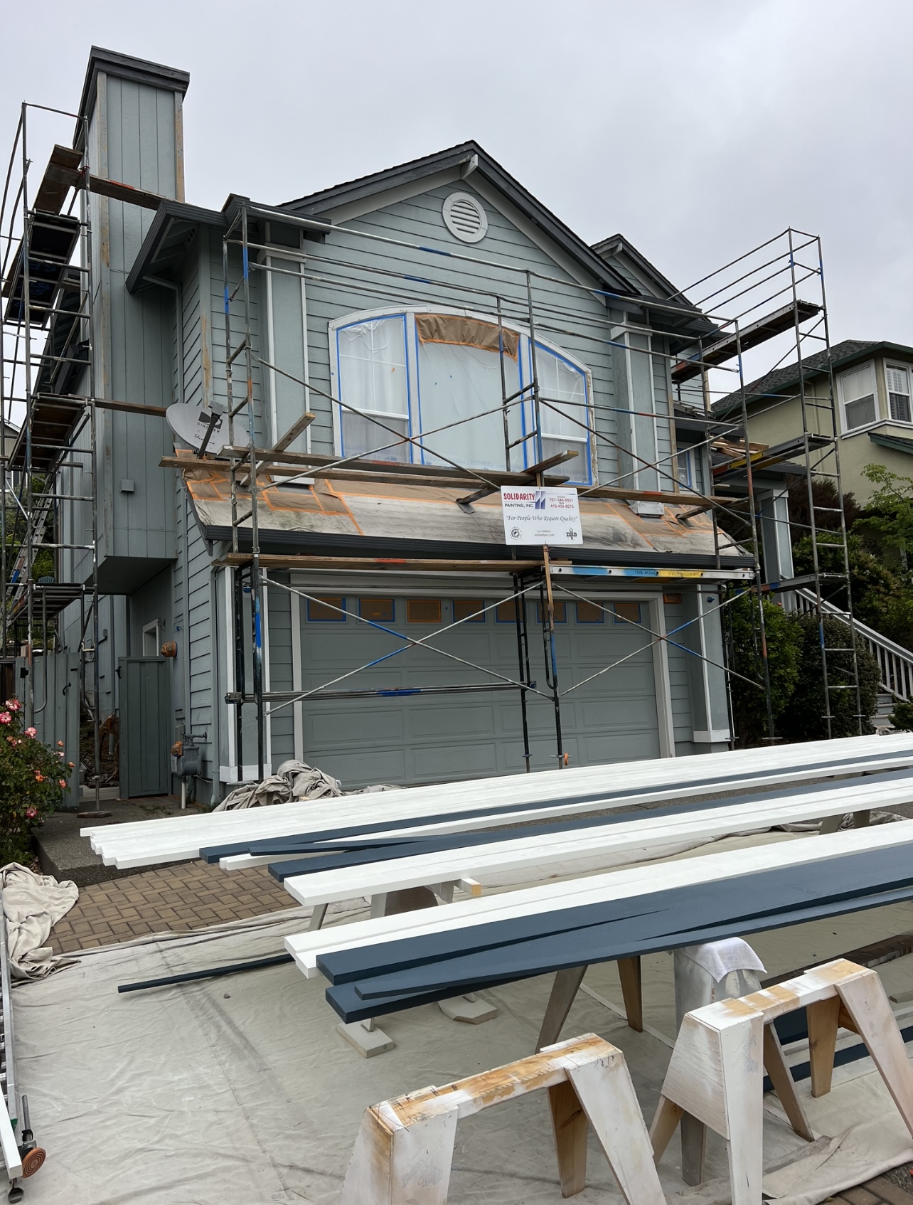 Scaffolded exterior mid-project: windows masked, and trim boards pre-finished on sawhorses before installation